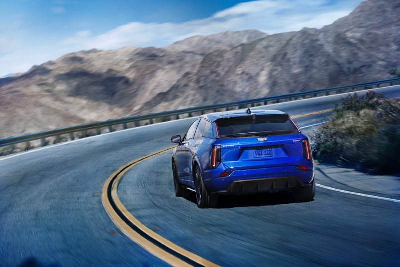 Rear View of a Blue 2026 OPTIQ-V Driving on a Curve of a Mountain Row | Cadillac of Jackson in Ridgeland MS